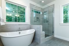 a white bath tub sitting in a bathroom next to a shower and two windows on the wall