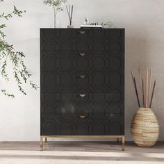 a black and gold cabinet next to a vase with plants in it on the floor