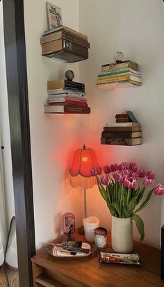 a table with a lamp and some books on it next to a vase filled with tulips