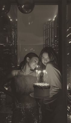 two women standing next to each other in front of a cake with candles on it