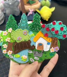 someone is holding up a small piece of felt that looks like a house in the woods