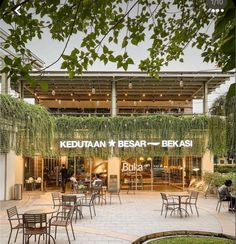 an outdoor restaurant with tables and chairs in front of the building that has plants growing on it