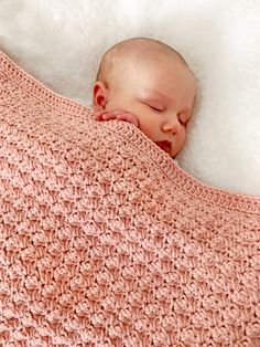 a baby sleeping on top of a pink crocheted blanket in the shape of a heart