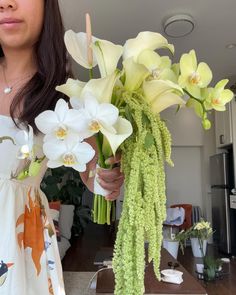 a woman holding flowers in her hands and standing next to a vase filled with white orchids