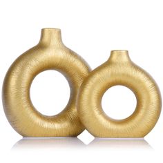 two gold colored vases sitting side by side on a white surface, one is shaped like an ovoid