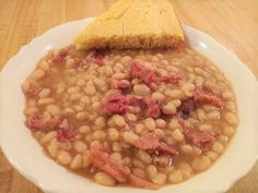 a white bowl filled with beans next to a piece of bread on top of a wooden table