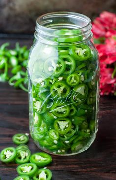 a jar filled with green peppers sitting on top of a wooden table