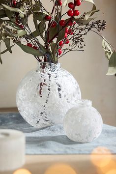 a glass vase filled with red berries and greenery on top of a blue table cloth