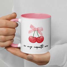 a woman holding a pink and white coffee mug with two cherries on it