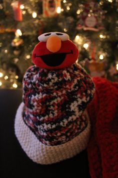 a knitted hat with an elmo face on it next to a christmas tree