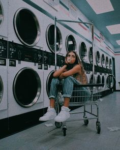 a woman sitting on top of a shopping cart in front of washers