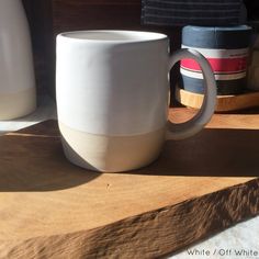 a white coffee cup sitting on top of a wooden table next to two other cups