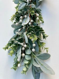 a bunch of green leaves and white berries hanging from a branch on the side of a wall