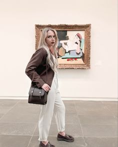 a woman standing in front of a painting holding a purse and looking at the camera