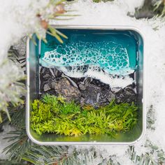 a christmas ornament hanging from a tree with water and rocks in the snow