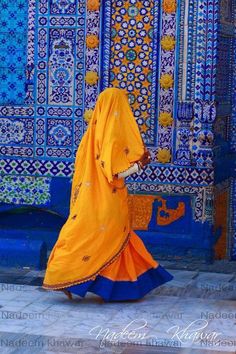 a woman in an orange and blue outfit walking past a wall with tiles on it