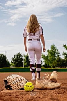 a softball and glove on the ground with a woman in the background looking at it