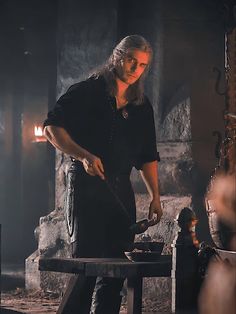 a woman cooking food on top of a stove next to a wooden table in a dark room