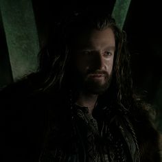 a man with long hair and beard standing in the dark, wearing a fur coat