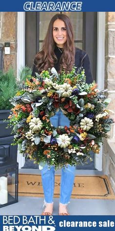 a woman standing in front of a door holding a wreath with flowers on it and the words bed bath beyond