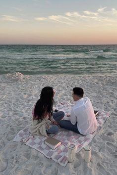 a man and woman sitting on a blanket at the beach