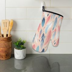 an oven mitt hanging on the wall next to a potted plant and spatula