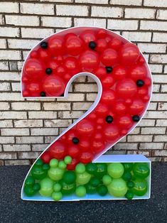 the number two is made out of red and green balloons in front of a brick wall