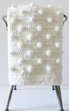 a white crocheted blanket sitting on top of a wooden chair with metal legs