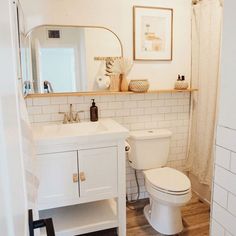 a white toilet sitting next to a sink in a bathroom under a mirror and framed pictures