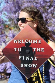 a woman holding up a sign that says welcome to the final show in front of purple flowers