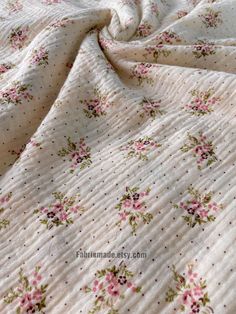 a white bed with pink and green flowers on it's comforter, next to a pillow