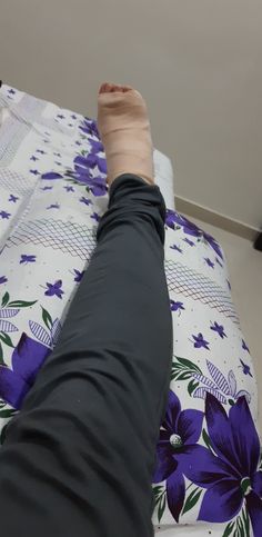 a person's leg and foot on a bed with purple flowered bedspread