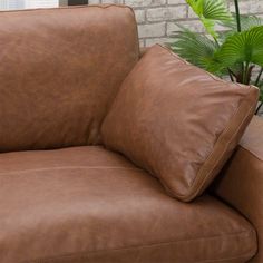 a brown leather chair sitting in front of a brick wall next to a potted plant