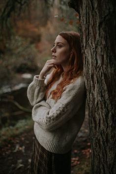 a woman leaning against a tree in the woods