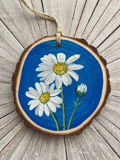 a blue and white painted wooden ornament with three daisies on it's side