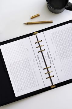 a black binder sitting on top of a table next to a coffee cup and pen