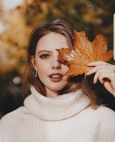 a woman holding a leaf in front of her face with the caption, autumn is here