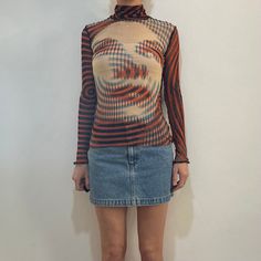 Iconic 1990s Jean Paul Gaultier mesh long sleeve club kid top with turtleneck.  This is a classic and wonderful Gaultier print pattern - in orange, turquoise, blue and black.  An important piece.  Felted irregular seams.  Label Jean Paul Gaultier, Maille Femme, 100% Nylon. Please hand wash cool, drip dry.  New vintage condition with no fabric or sewing flaws.  Measurements - very stretchy, measurements made without stretch Shoulders 33cm/ 13inches Chest 80cm/ 31inches Waist 60cm/ 24inche Shoulder to hem 65cm/ 26inches Sleeve length 60cm/ 24inches Models measurements Shoulders 42cm/ 16.5inches Chest 84cm/ 33inches Waist 66cm/ 26inches Hips 92cm/ 36inches Height 175cm/ 5'9'' Multicolor Long Sleeve Mesh Top With Graphic Print, Long Sleeve Graphic Print Mesh Top For Party, Long Sleeve Mesh Top With Graphic Print For Party, Multicolor Sheer Long Sleeve Top, Fitted Multicolor Mesh Top With Long Sleeves, Fall Party Graphic Print Mesh Top, Fall Party Mesh Top With Graphic Print, Multicolor Long Sleeve Mesh Top For Fall, Fitted Graphic Print Mesh Top For Fall