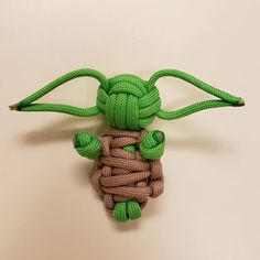 a green stuffed animal is tied up to a white wall with brown and green cords