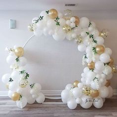 a white and gold balloon arch decorated with greenery