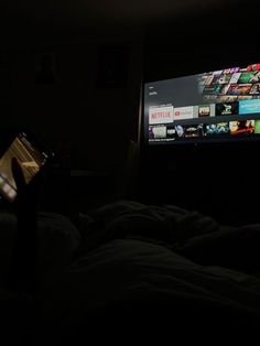 a flat screen tv sitting on top of a bed in a dark room next to a remote control