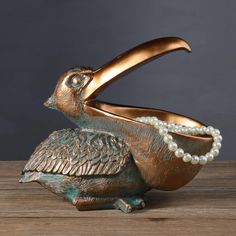 a bronze bird with pearls on its beak is sitting on a table next to a bowl