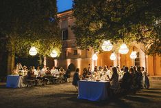 a group of people sitting at tables in front of a building with lights on it