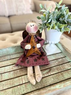 a doll sitting on top of a wooden table next to a potted plant