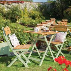 an outdoor table and chairs set up in the grass with flowers around it, along with potted plants