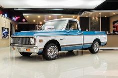 an old blue and white truck in a showroom with neon signs on the walls