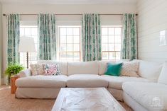 a living room with white couches and pillows on top of the couch, along with two large windows