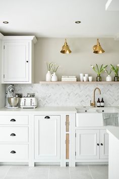 a kitchen with white cabinets and gold accents on the counter tops, along with brass pendant lights