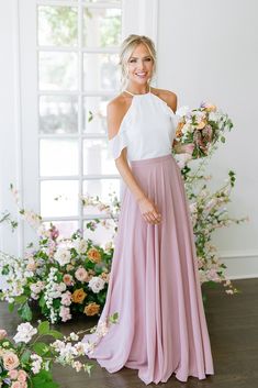 a woman standing in front of flowers wearing a pink skirt