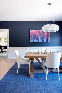 a dining room with blue walls, white chairs and a wooden table in the center